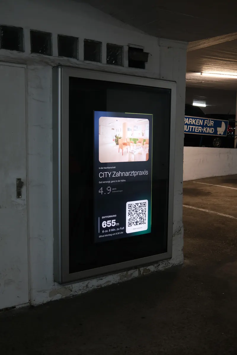 Bildschirm in einem Schaukasten an der Einfahrt des Parkhauses am Weberplatz, darauf die CITY Zahnarztpraxis, 655 Meter entfernt